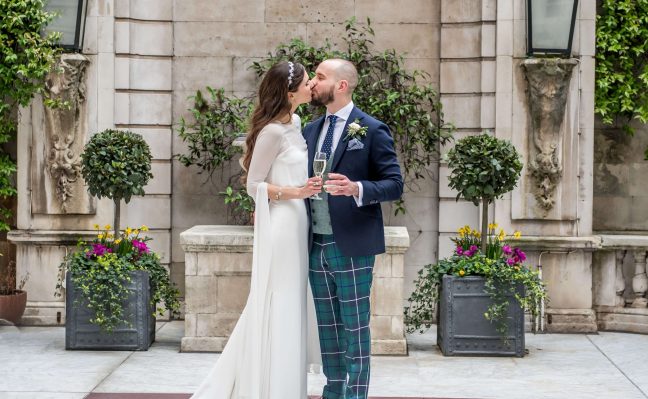 A joyful moment as the bride and groom kiss, framed by a picturesque fountain, celebrating their love and commitment.
